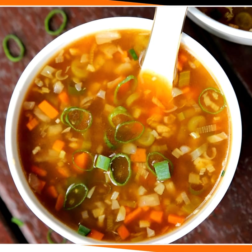 Close-up of a white bowl filled with Indian vegetable soup, garnished with green onions.
