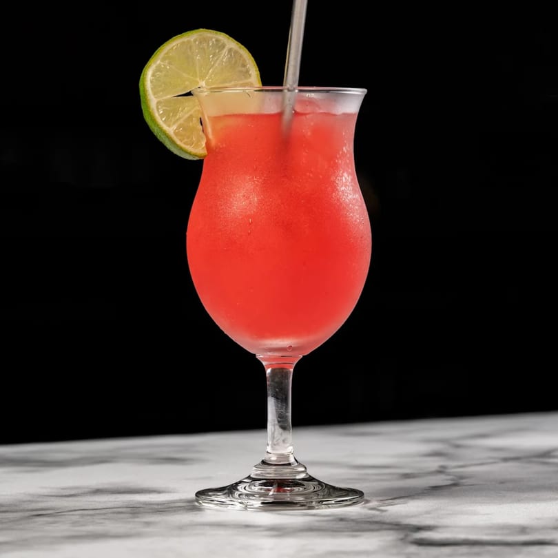 A vibrant red cocktail in a hurricane glass, garnished with a lime slice and a straw.