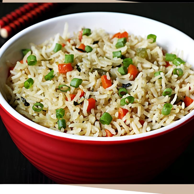 Close-up of Indian fried rice with carrots and green onions in a red and white bowl.