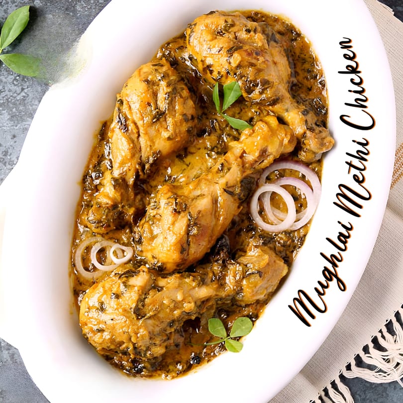 Mughlai Methi Chicken, an Indian dish, in a white oval bowl with onion rings and green garnish.