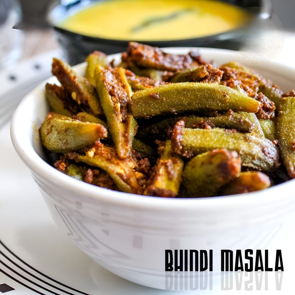 A white bowl filled with Bhindi Masala, a spicy Indian okra dish, with a yellow curry in the background.