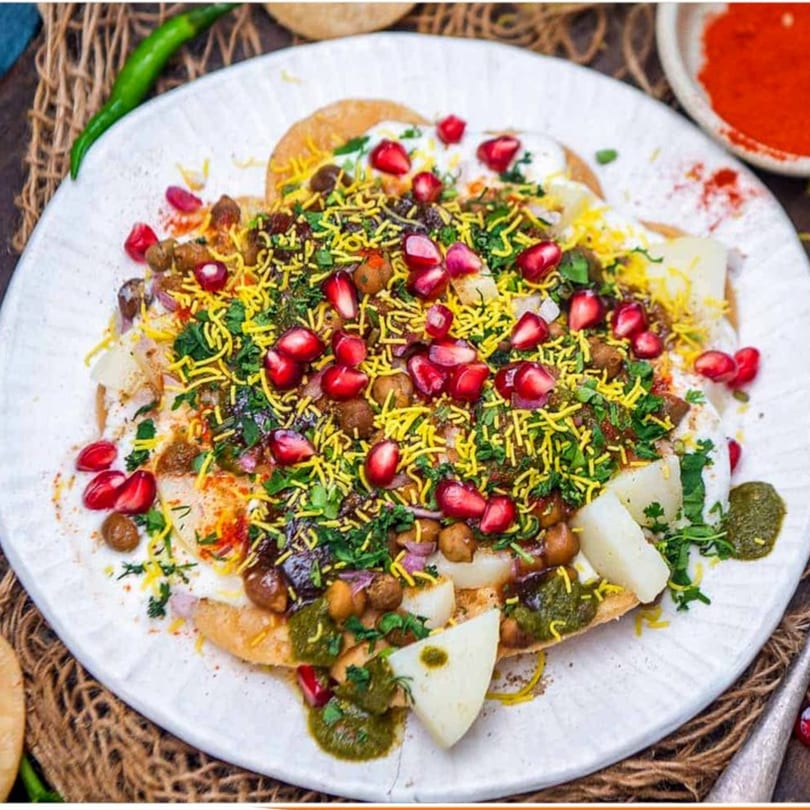 Close-up of Indian chaat with pomegranate, sev, chickpeas, and sauces on a white plate.